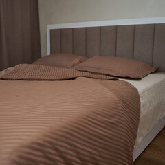 A large bed with light brown bedding(linens).