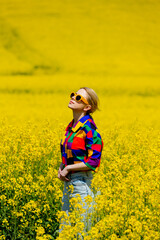 Beautiful female in 90s stylish shirt in rapeseed field