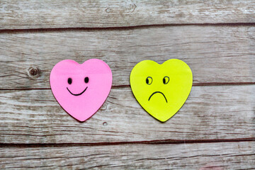 Paper hearts sticky notes with happy and sad faces on wooden background .Happiness vs depression...