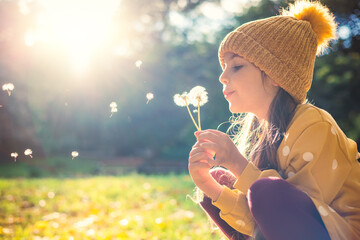 Little beautiful girl blowing dandelion on the meadow at sunset - 463977342