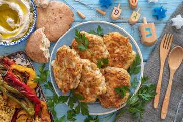 Chicken shawarma latkes, pita bread, grilled vegetables, wooden dreidels for Jewish holiday Hanukkah on blue background. Hebrew letters on dreidels say: 