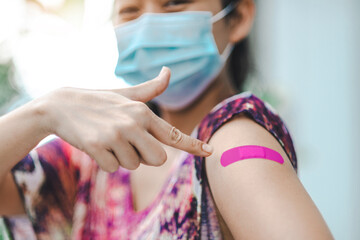 A healthy tourist woman pointing to her pink Plaster Bandage after getting the corona vaccine vaccinated immunity is wearing a protective face mask. Vaccination inoculation concept. Selective focus