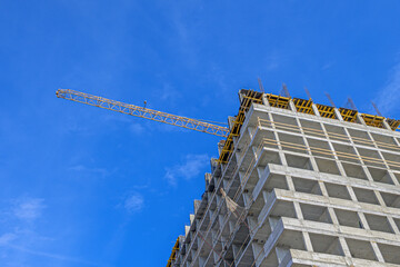 Boom of a construction crane over a house under construction against a blue sky background