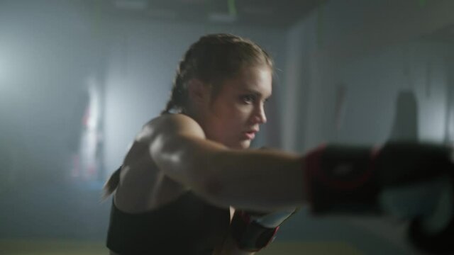 Woman power, female fighter trains his punches, beats a punching bag, training day in the boxing gym, the female strikes fast, 4k slow motion.