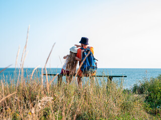 Happy father and daughter sitting on bench on marine landscape back view. Dad and child having fun walking together looking at the sea from above.Lifestyle real people. Happiness family travel concept