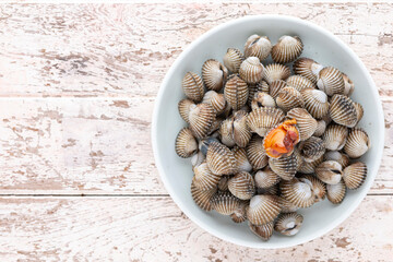 fresh steamed cockles, boiled cockles in ceramic plate on old white wood texture background with copy space for text, top view, light and airy food photography, blood cockle