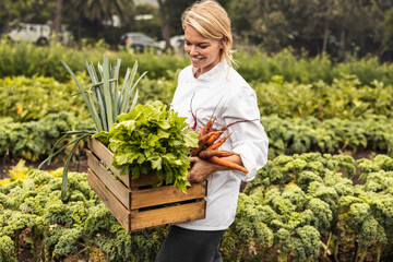 Smiling young chef carrying fresh vegetables on a farm