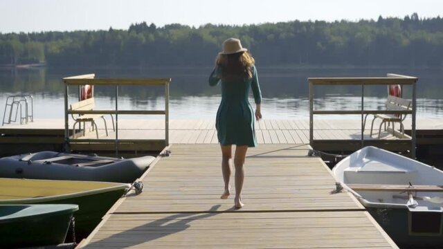 Woman preparing for jumping into the lake from wooden pier. Having fun on summer day on the vacations. Young girl runs and undresses for swiming in the the water from the dock.