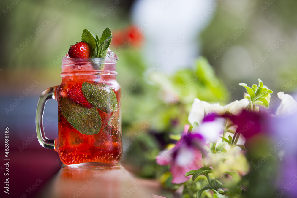 Poster closeup shot of cold fruit tea in a mason jar on a wooden surface with beautiful flowers