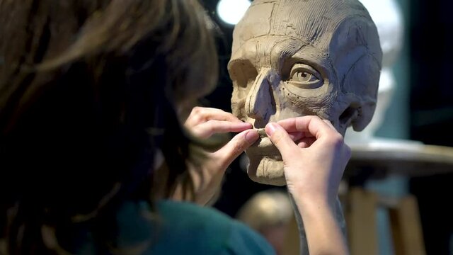 Woman sculptor at work on a sculpture of a human head. The process of restoring the shape of the lips. Side view. Close up view.