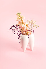 White big tooth vase with flowers on pink background. Work and orthodontist dentist aesthetics.