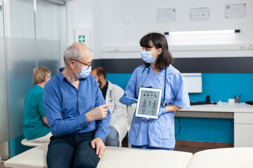 Nurse holding digital tablet with human skeleton on image for elder patient. Medical assistant explaining osteopathy diagnosis and rehabilitation with device to cure retired man.