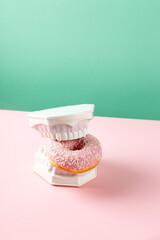 Plastic jaws hold sweet pink donut in teeth. Dental health, dentistry and caries concept. Colored creative art.