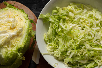 green young cabbage cut in a bowl and on a wooden board, cabbage salad on a wooden table © Виктория Котлярчук