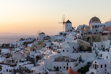 Oia, Santorini, Greece - June 28, 2021: Whitewashed houses and windmills in Oia in warm rays of sunset on Santorini island. Greece