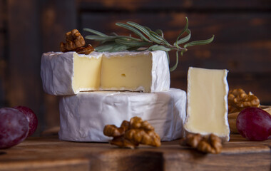Cheese with white mold, nuts on a wooden cutting board.