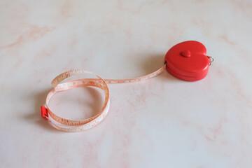 Tape measure in the heart shape on the pink marble background.