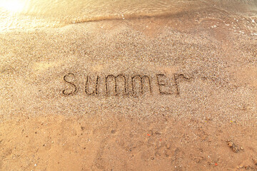The word Summer is written on the sandy seashore