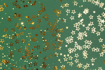 Trendy gold colored glittering stars confetti scattered on a green background.