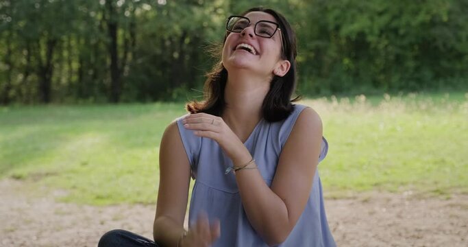 Happy young woman watching video online with smartphone in city park. Girl looking at screen of mobile telephone and laughing for funny movie. Girl with cell phone outdoors
