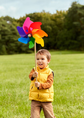 childhood, leisure and people concept - happy little boy with pinwheel playing at park