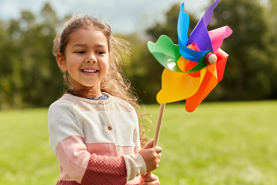 childhood, leisure and people concept - happy little girl with pinwheel playing at park