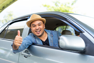 Handsome asian man wear hat the blue jeen shirt is driving and thumbs up sitting on car seat...