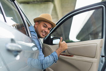 Handsome asian man wear hat the blue jeen shirt is driving and thumbs up sitting on car seat showing thumb up and fastening seat belt. Car safety, insurance, buying and selling cars, travel concept.