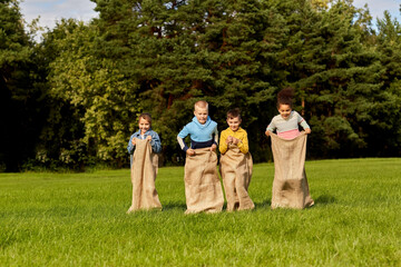 Obraz premium childhood, leisure and people concept - group of happy children playing bag jumping game at park