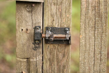 Photo of a homemade metal latch on an old wooden gate. An old metal shutter on an unpainted wooden fence. Locked lock