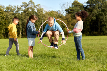 childhood, leisure and people concept - group of happy children jumping through hula hoop at park