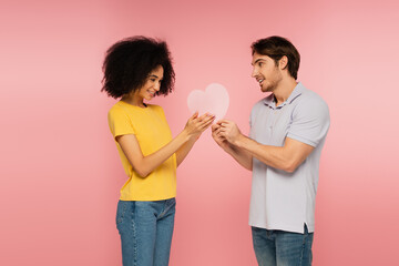 man presenting paper heart to young and pretty hispanic woman isolated on pink.