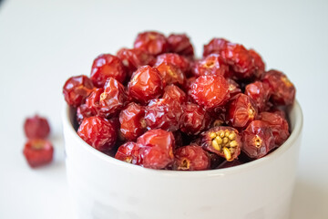 Sun-dried wild rose hip in a white bowl on white background