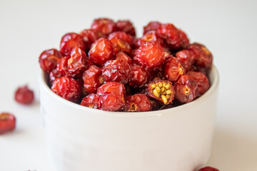 Sun-dried wild rose hip in a white bowl on white background