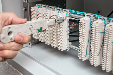 A man electrician checks the terminals of telephone communication equipment. The specialist serves the node of the telephone line. Authentic work-like scene.