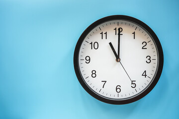 Classic black and white analog clock on blue background at Eleven o'clock with copy space