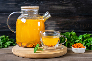 Teapot and cup of delicious and aromatic sea buckthorn tea with mint and honey on wooden table Useful has anti-inflammatory and antistress effects Winter hot vitamin drink concept