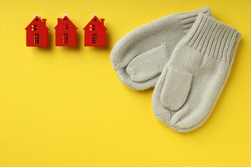 Concept of heating season with mittens and red houses on yellow background