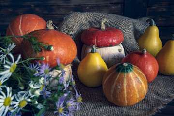 Pumpkins and a bouquet of wildflowers lie on rough burlap on a wooden background.