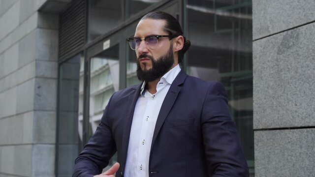 Self confident egoistic man in eyeglasses adjusting his blazer standing outdoor