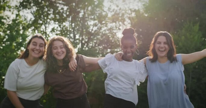 Youth culture with happy young people, group of female friends in park. Multiethnic teens outdoors, women smiling and laughing. Portrait of teenagers together, girls looking at camera. Slow motion