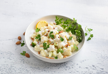 Cauliflower salad with apples, almonds, herbs and yogurt dressing on light gray textured background. Healthy homemade diet food