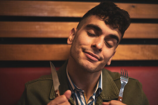 a young man posing with a knife and fork in a restaurant.