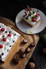 impressive piece of cake decorated with whipped cream and grapes, raspberries, red leaves, chestnuts, on black wooden table