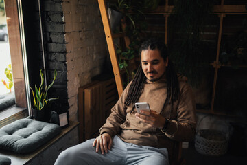 Young man hipster using his smartphone, sitting in a coffeehouse and drinking coffee.