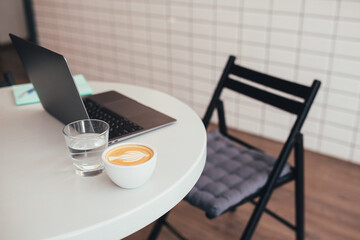 Cup with fresh coffee cappuccino and laptop on a white table.