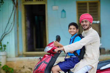 Young indian farmer dropping his child to school on bike