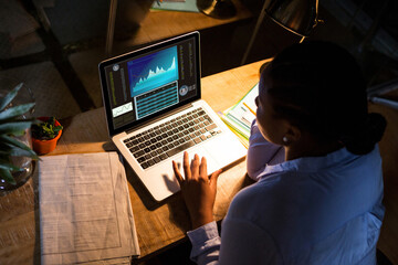 Biracial businesswoman sitting at desk, using laptop with statistical data on screen