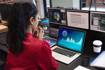 Biracial businesswoman sitting at desk using laptop with graph and statistical data on screen