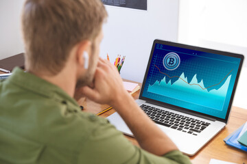 Caucasian businessman sitting at desk, using laptop with statistical data on screen